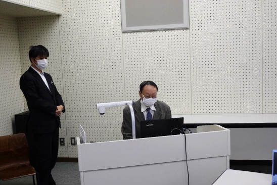 シンポジウム冒頭で挨拶する伊藤雅道総合研究所長（右）とZoom開催の技術的サポートを担った信太直己スポーツ科学部准教授（左）。